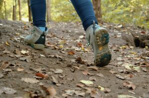 Close-up of a hiker's trekking shoes on a leaf-covered trail in autumn.