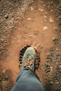 A single boot stepping into a muddy puddle outdoors, creating a splash on a dirt road.