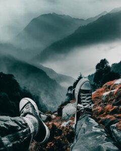 Foggy mountain view with legs in sneakers, embracing adventure and tranquility.
