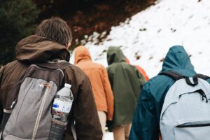 A group of hikers with backpacks walking on a snowy mountain trail in winter.