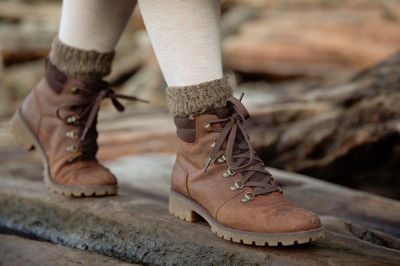 From above female feet in light tights and casual warm autumn boots standing on wooden log against shabby wooden planks