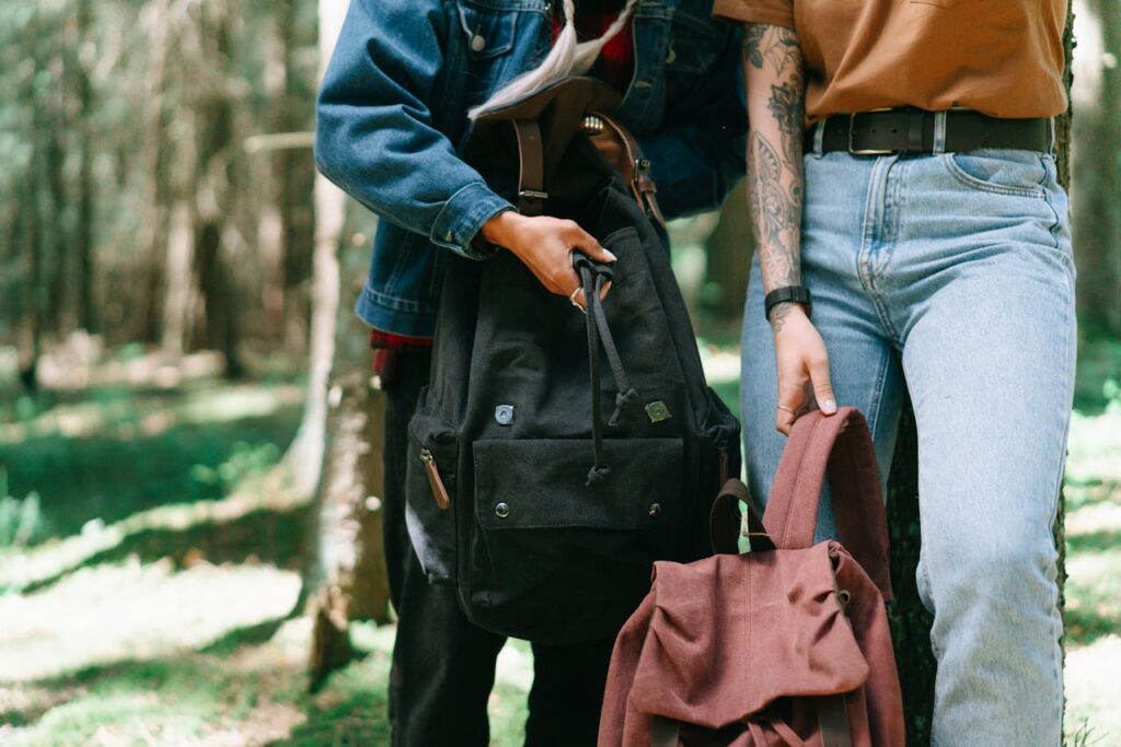 Two stylish backpackers with tattoos and jeans hiking through a lush green forest.